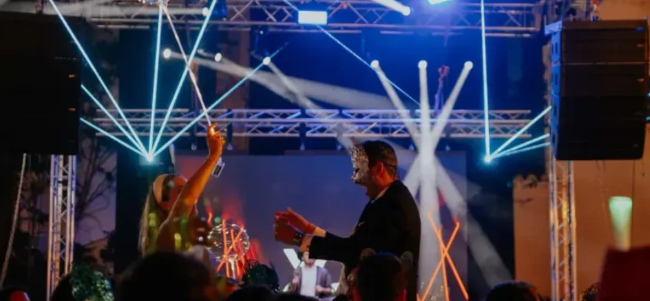 Invitados con máscaras bailando ante un escenario con focos, truss y pantalla LED