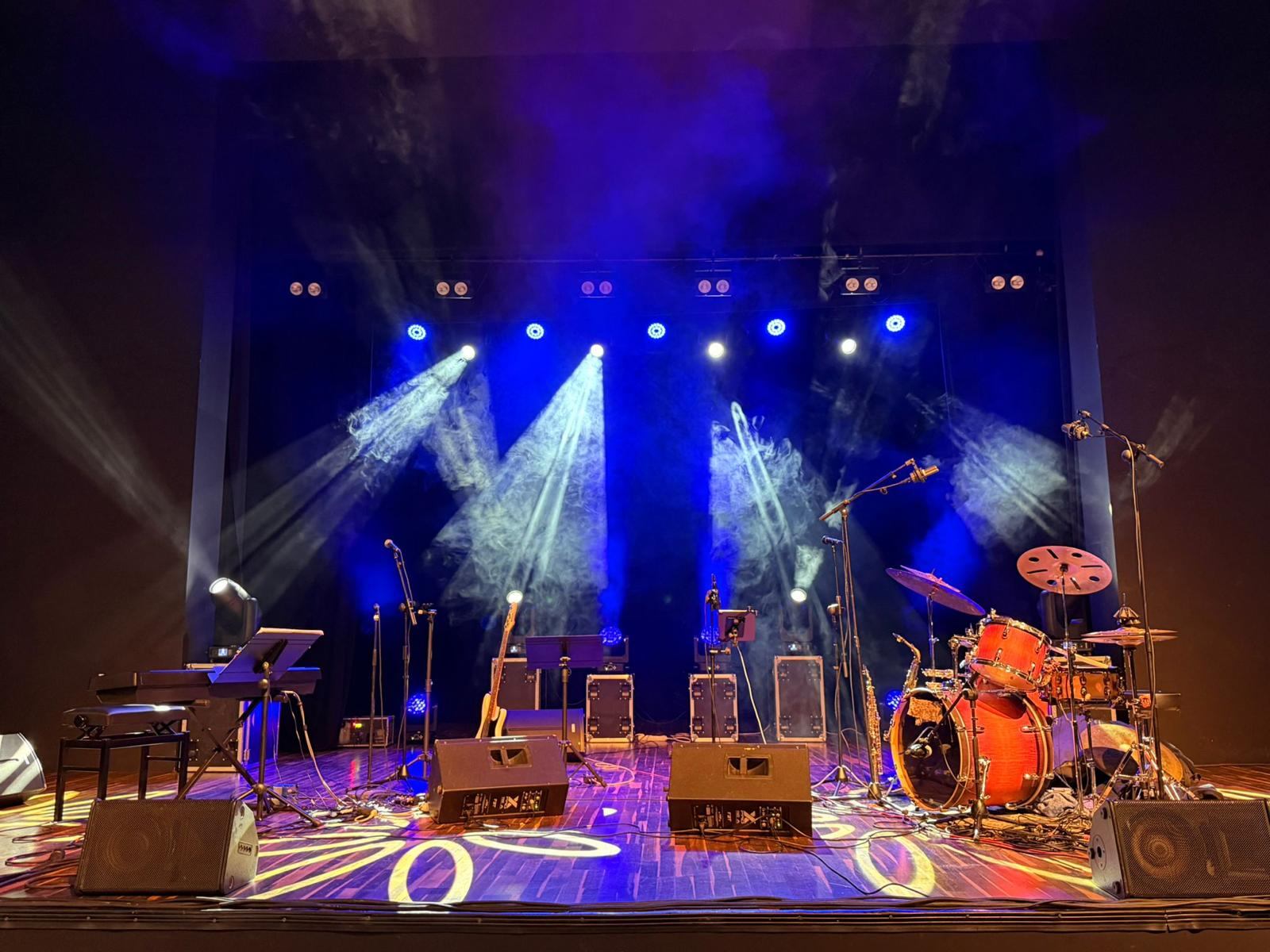 Escenario preparado para una actuación en directo con batería, amplificadores, monitores y focos azules