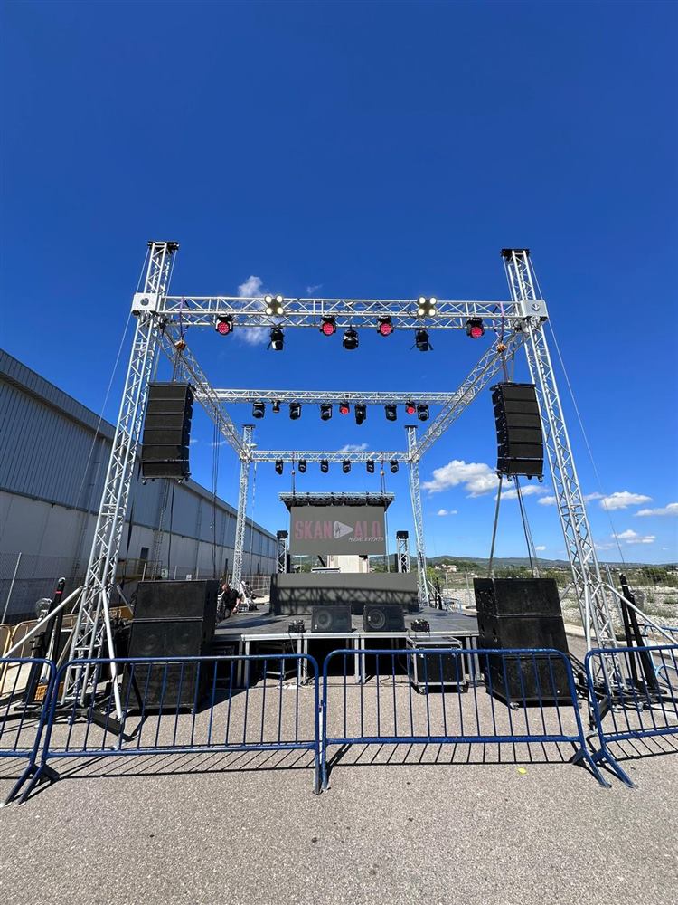 Escenario exterior con estructura de truss, altavoces line array y focos, a pleno día